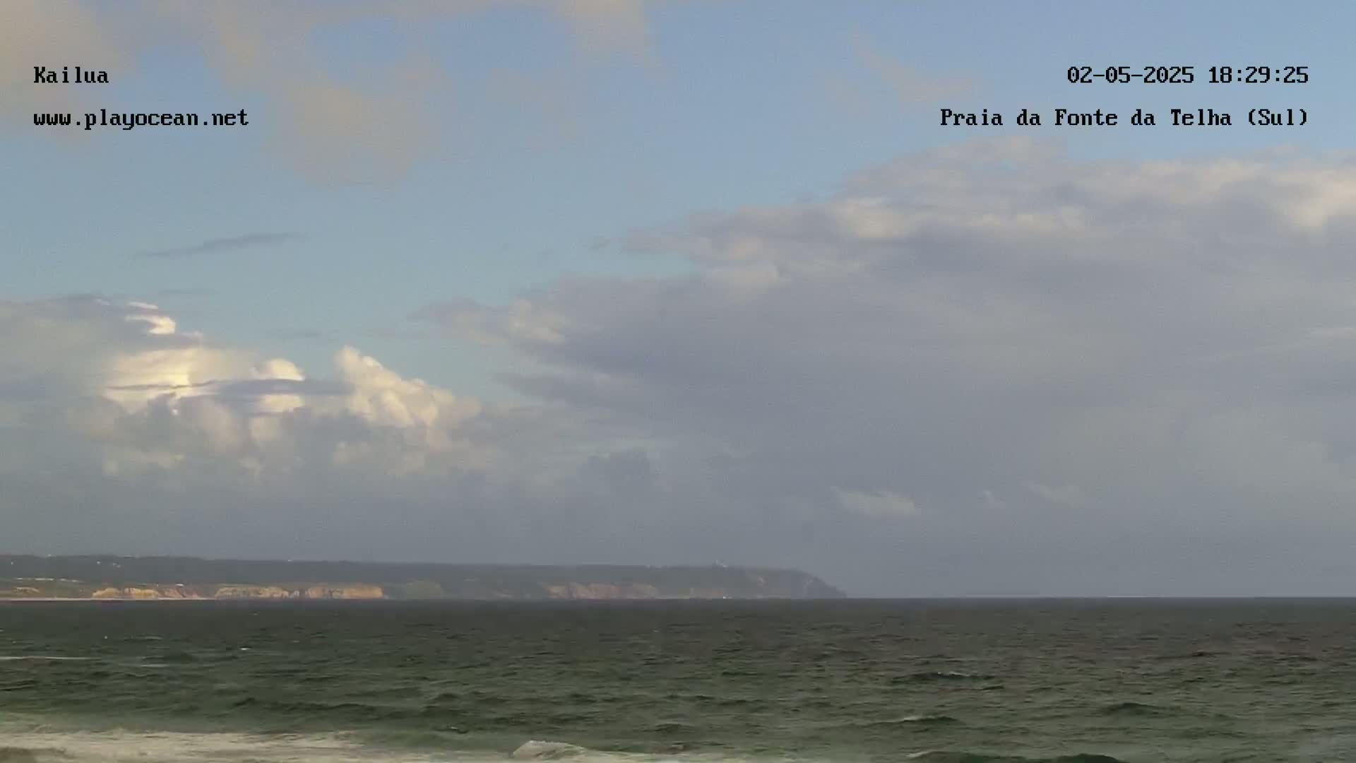 A partly cloudy sky overlooks a calm ocean with a distant coastline.