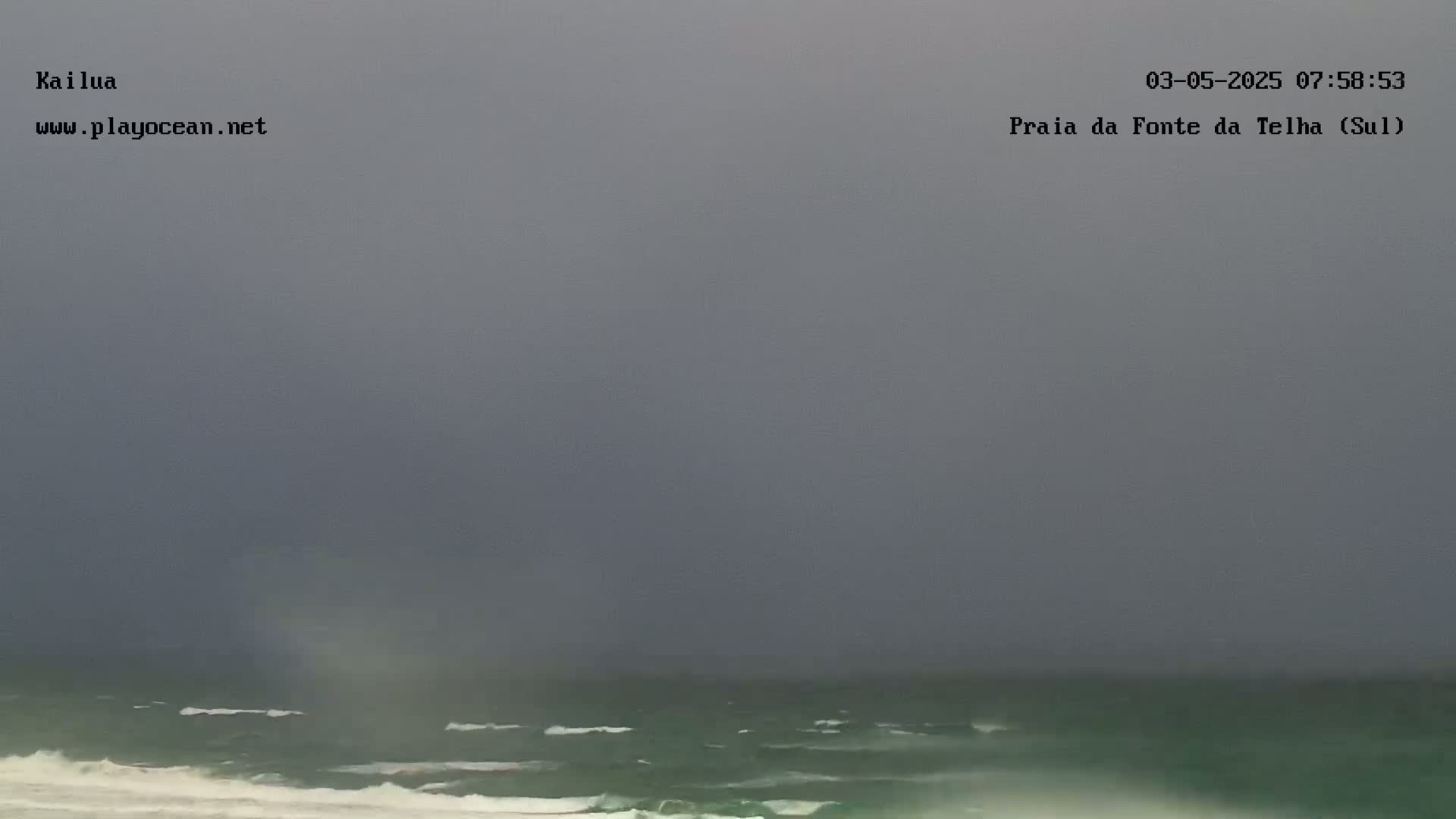A dark, overcast sky hangs over a choppy ocean with small waves breaking on the shore.