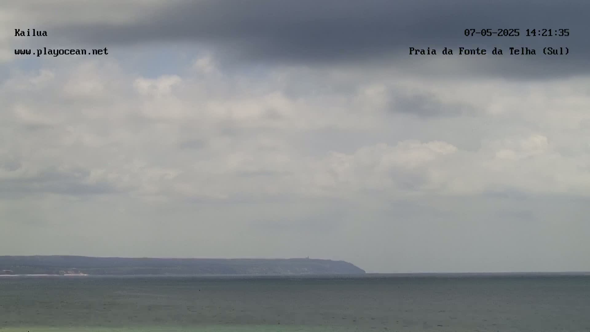 A calm ocean stretches to a distant landmass under a mostly cloudy sky.