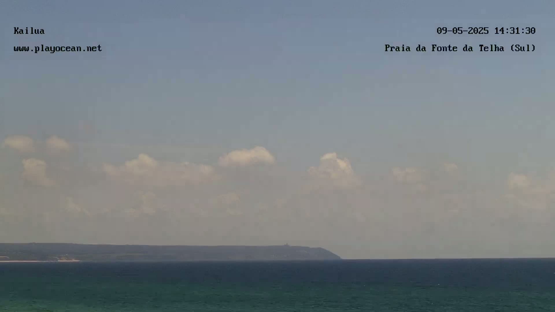 A calm ocean with a distant landmass under a partly cloudy sky.