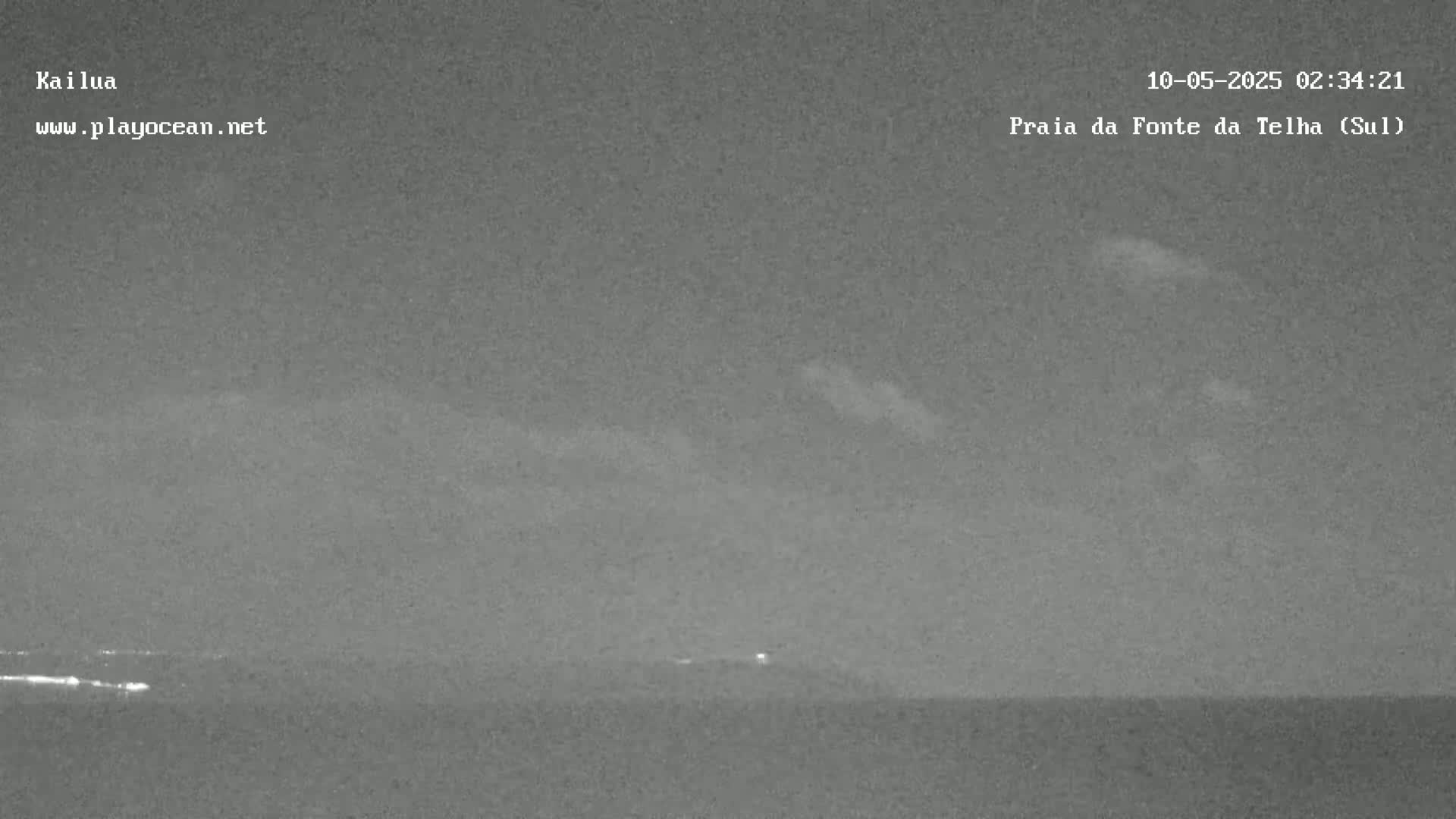 A nighttime, low-light image shows a dark ocean under a mostly clear sky with a few faint clouds.