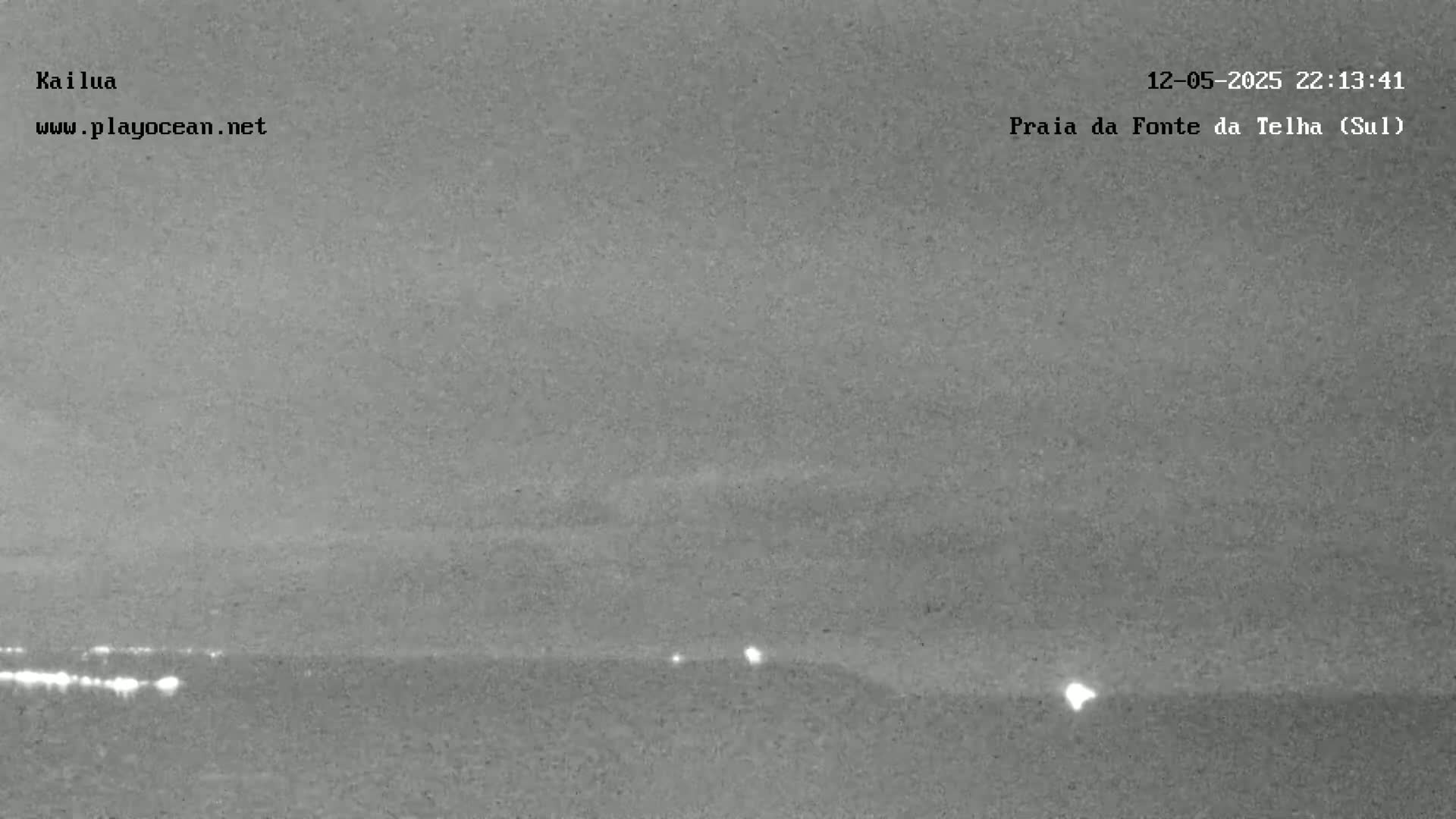 A nighttime, low-light image shows a dark, overcast sky over a dark horizon line with a few distant, faint lights visible.