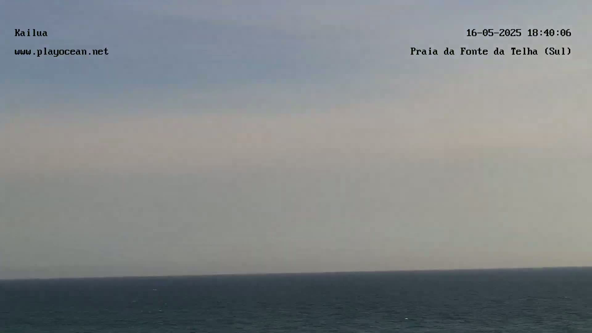 A calm ocean stretches to a hazy horizon under a pale, overcast sky.