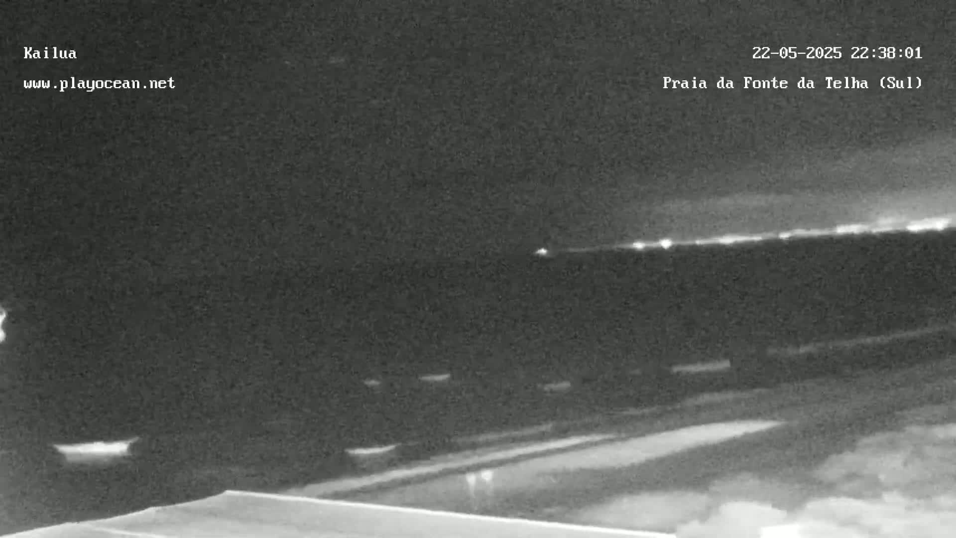 A nighttime, low-light view of a dark beach with a faint horizon line showing distant lights.