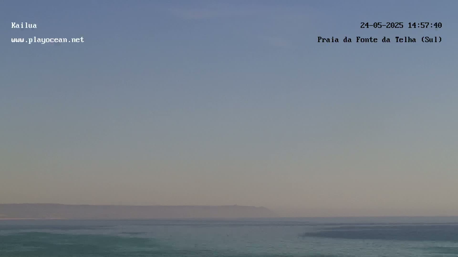 A hazy, calm ocean scene shows a distant landmass under a pale, clear sky.