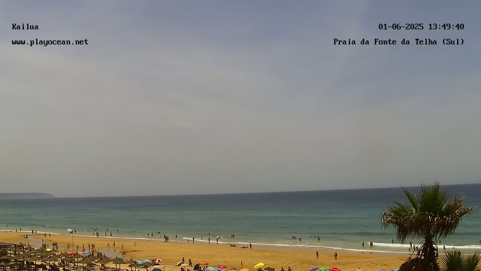 A sandy beach with people swimming and sunbathing under mostly sunny skies, overlooks a calm ocean.