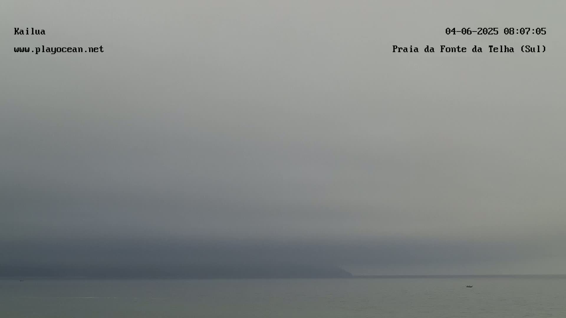 A hazy, overcast sky hangs over a calm body of water with a dark landmass barely visible in the distance.