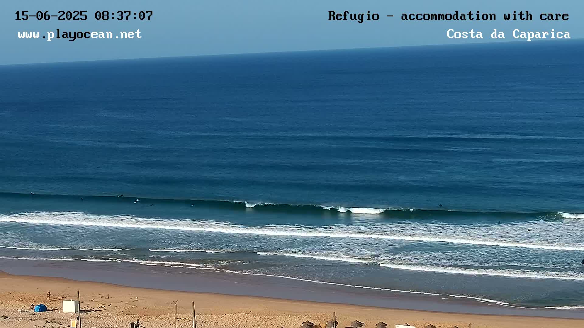 A sandy beach with several surfers in the ocean under a clear sky.