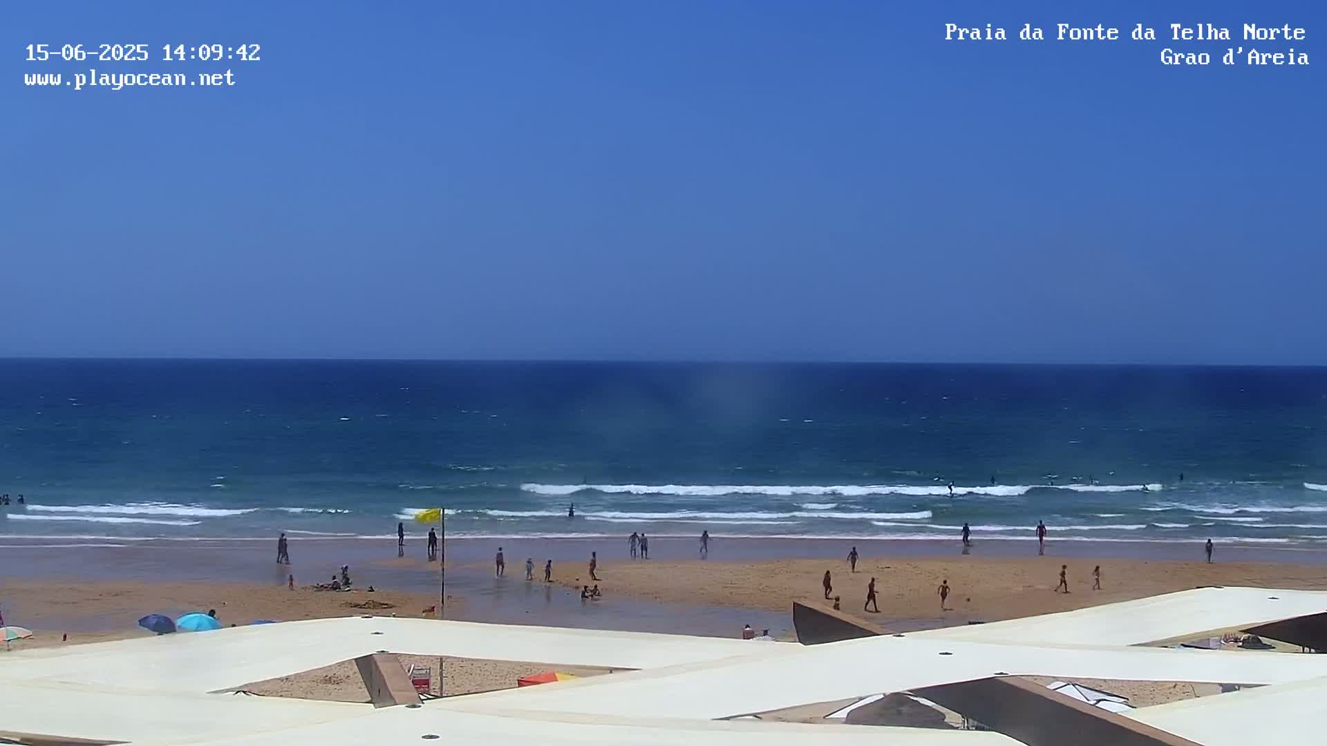 A sandy beach with people swimming and playing in the surf under a clear blue sky.