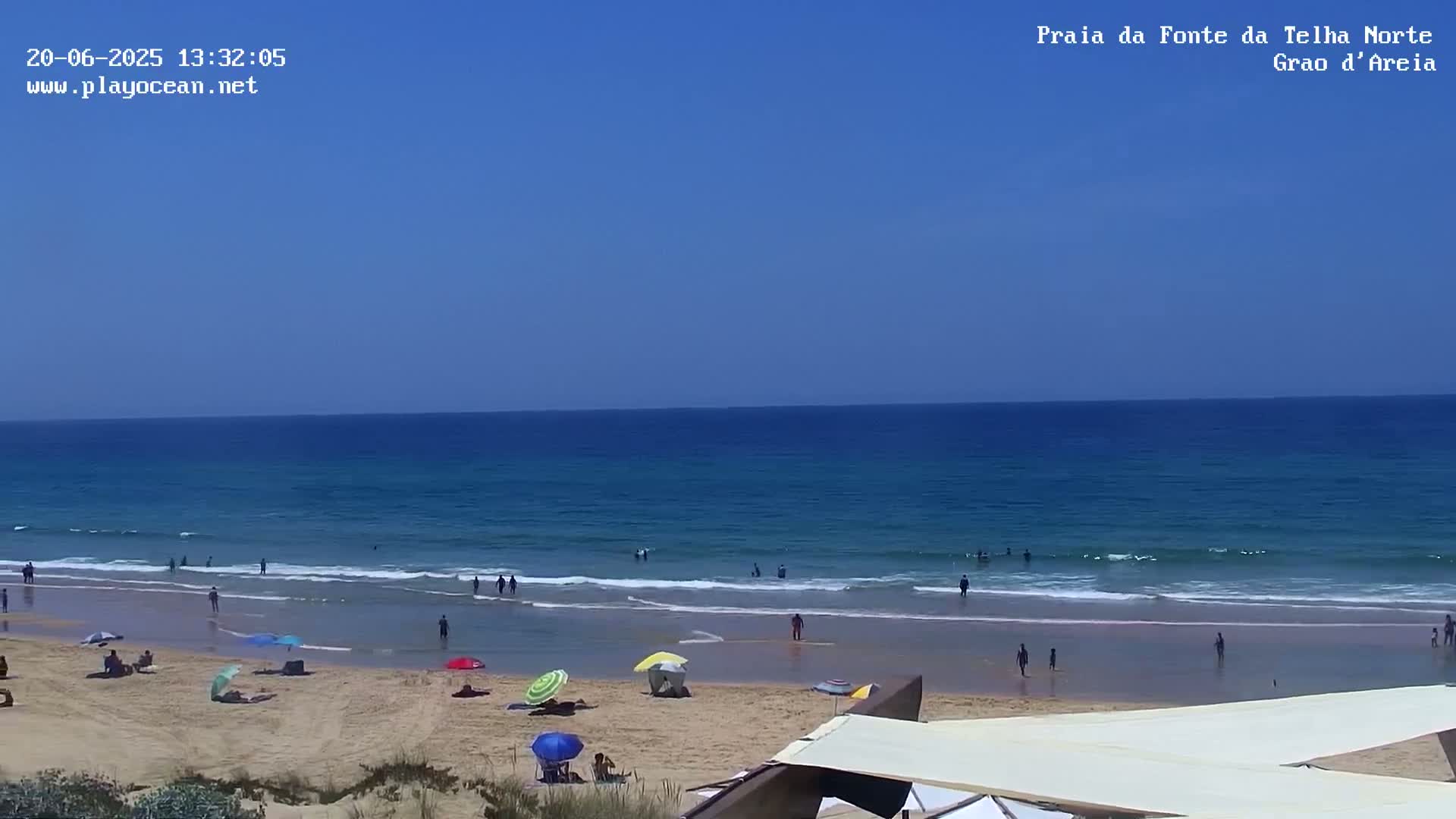 A sandy beach with people swimming and relaxing under umbrellas on a sunny day with a calm ocean.