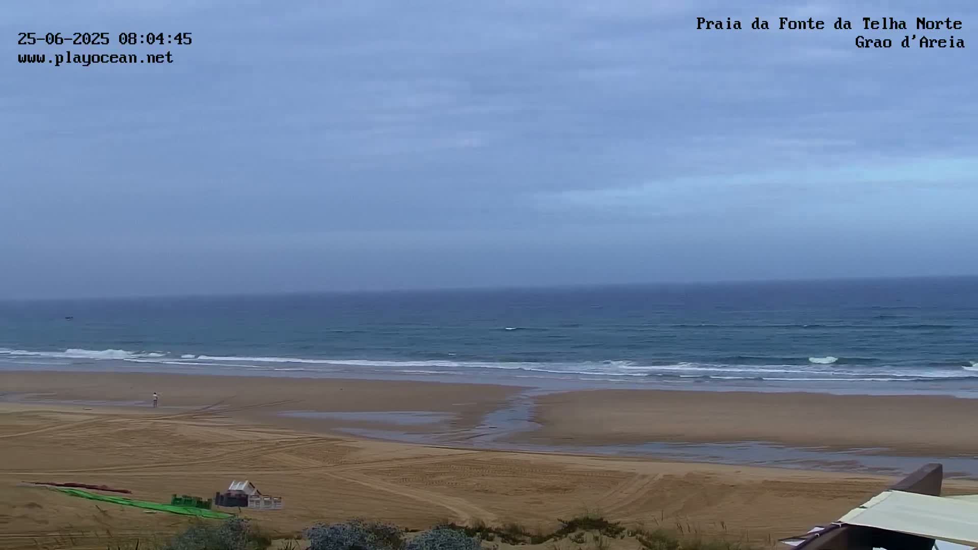 A mostly cloudy day reveals an expansive sandy beach meeting a calm, blue ocean with small waves.