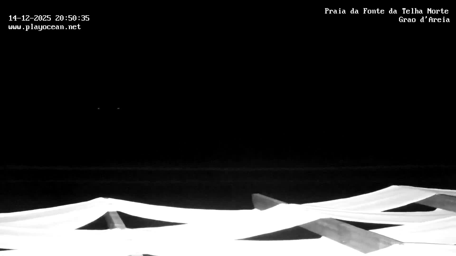 A sandy beach with small waves, numerous people, and beach umbrellas, overlooks a calm ocean under a clear blue sky.