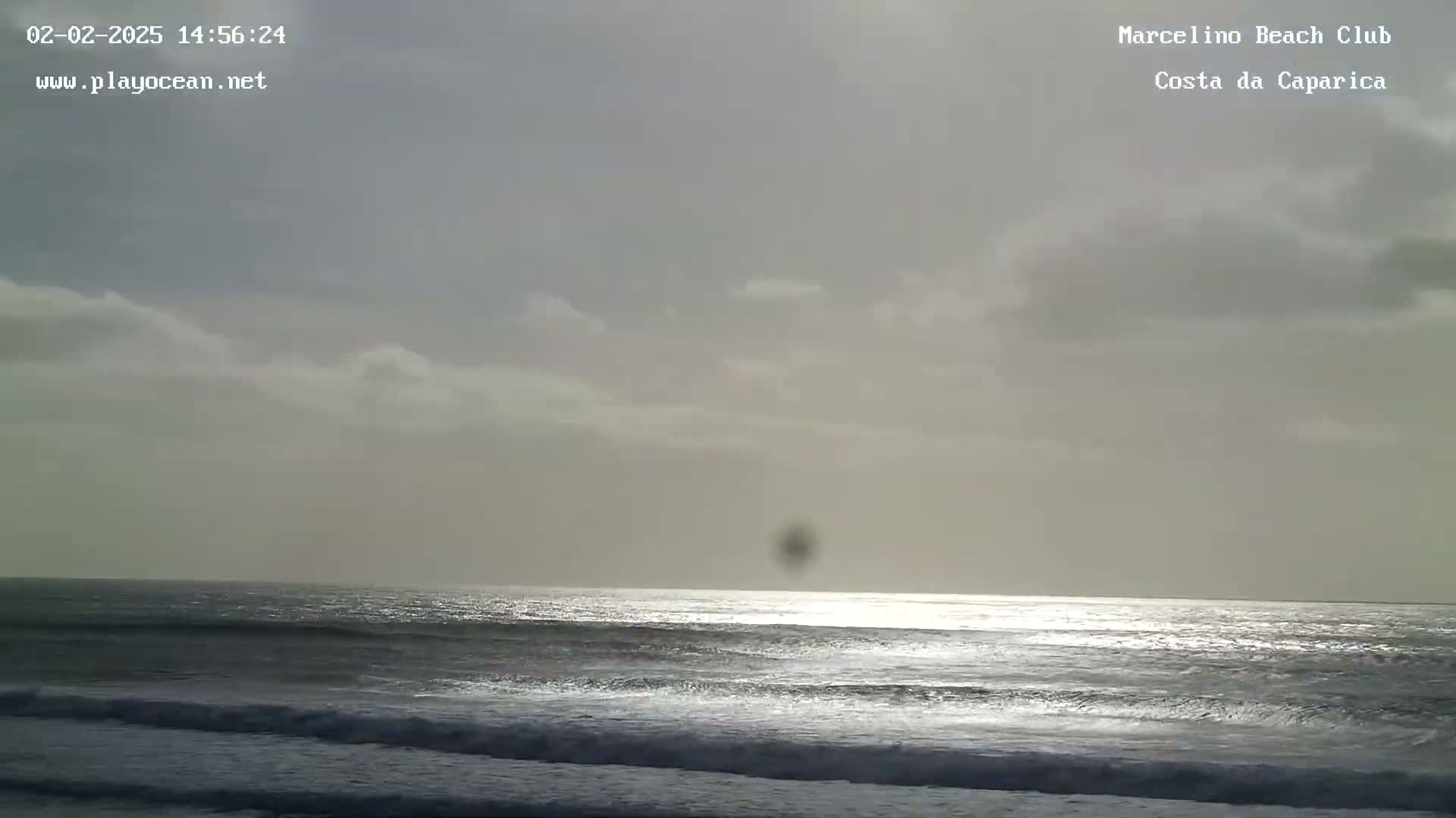 A mostly cloudy sky overlooks a dark, wavy ocean reflecting sunlight on its surface.