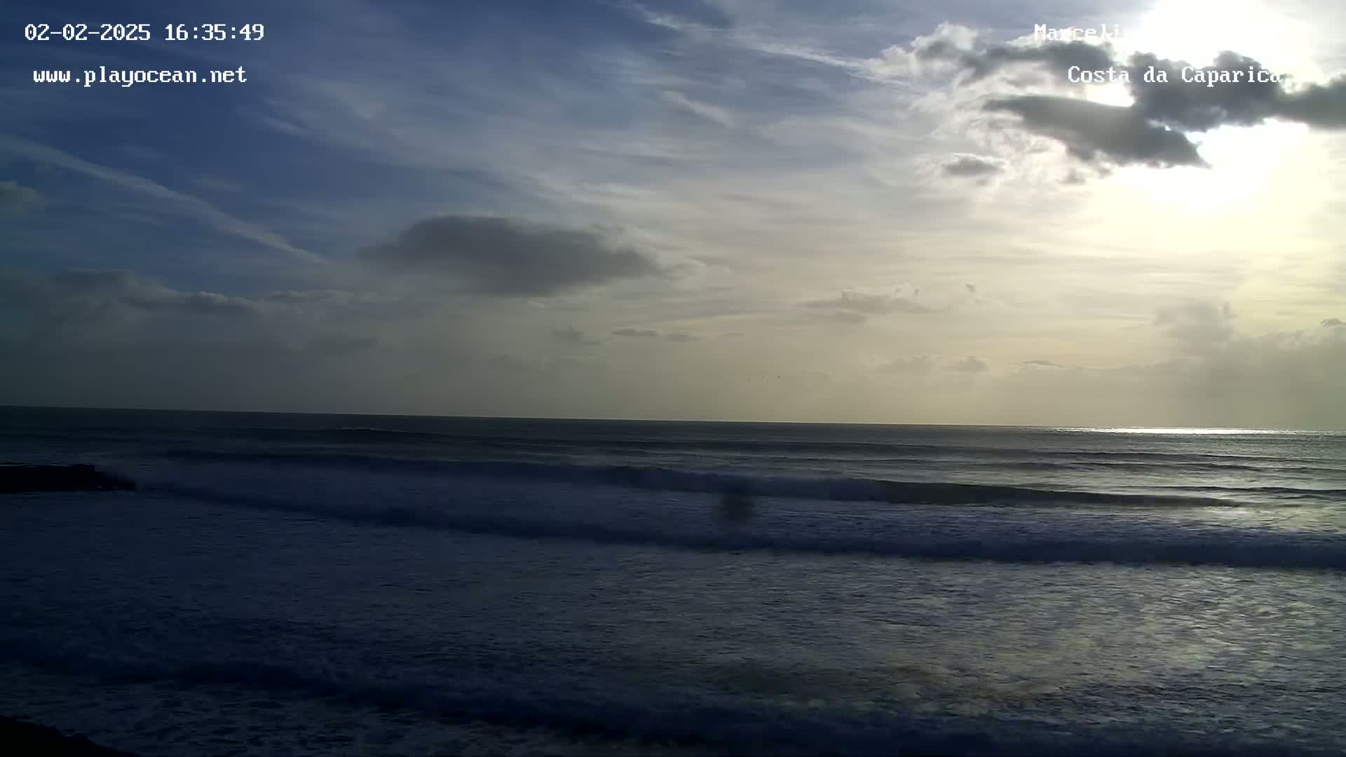 A partly cloudy sky illuminates a dark ocean with small waves rolling onto a beach.