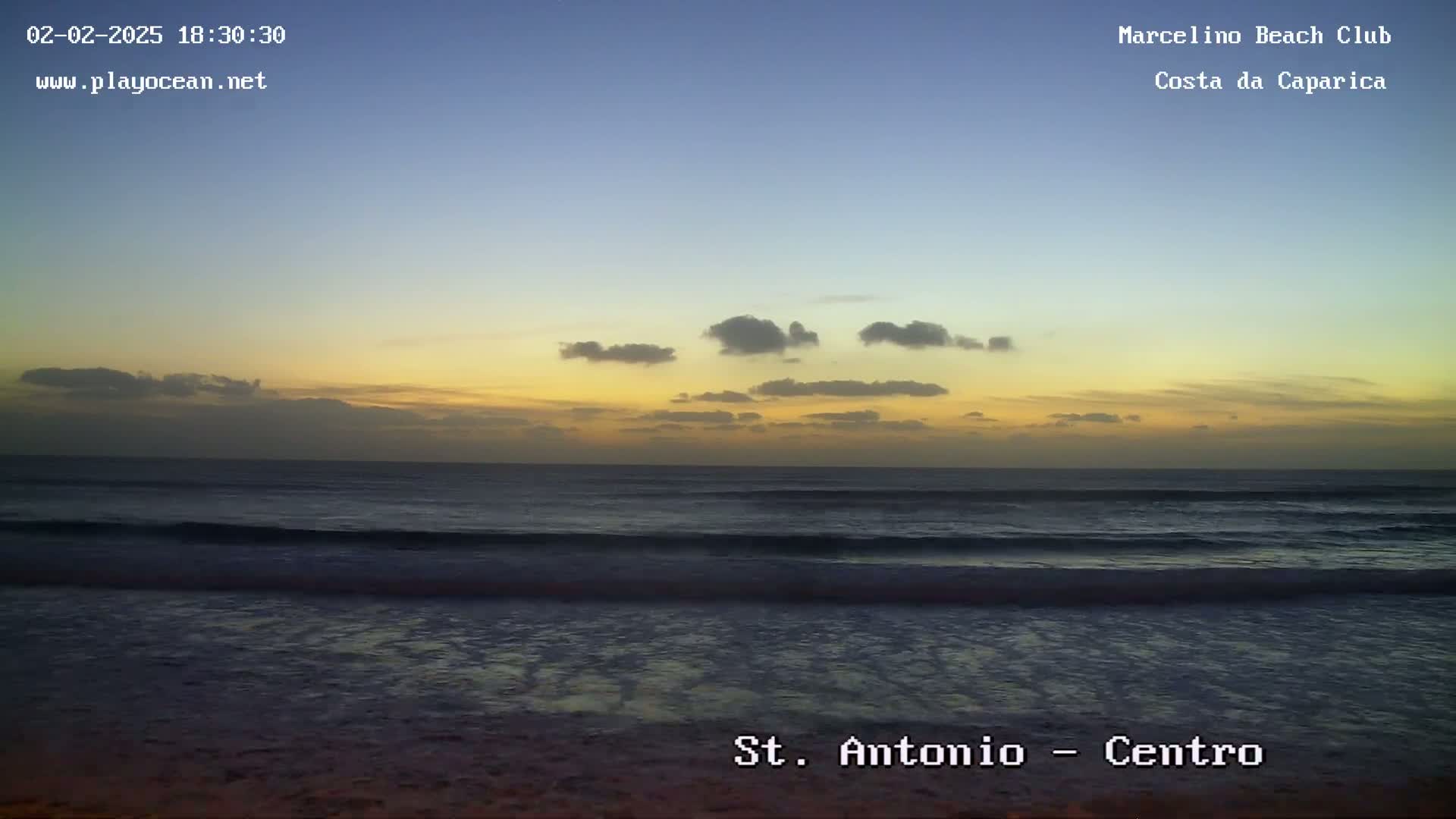 A beach at sunset shows a calm ocean with small waves under a partly cloudy sky.