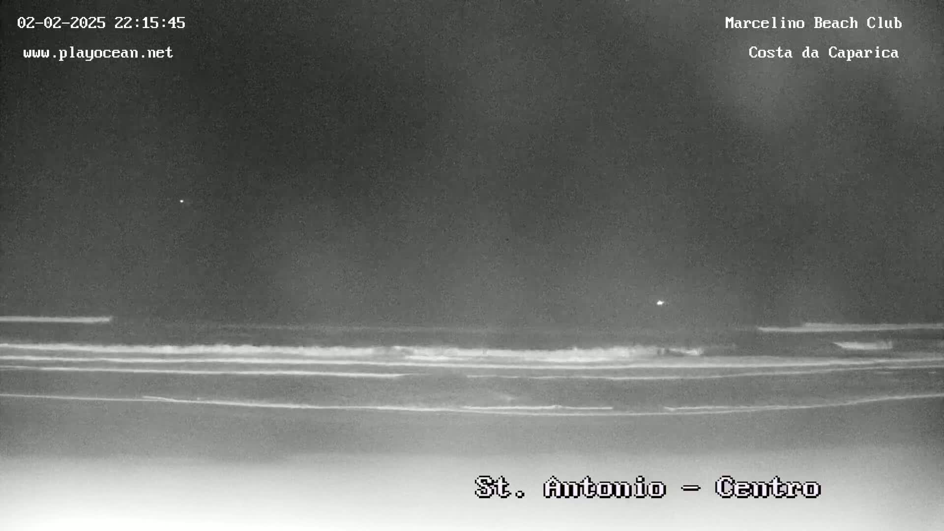 A nighttime, low-light image shows a dark ocean with small waves breaking on the shore.