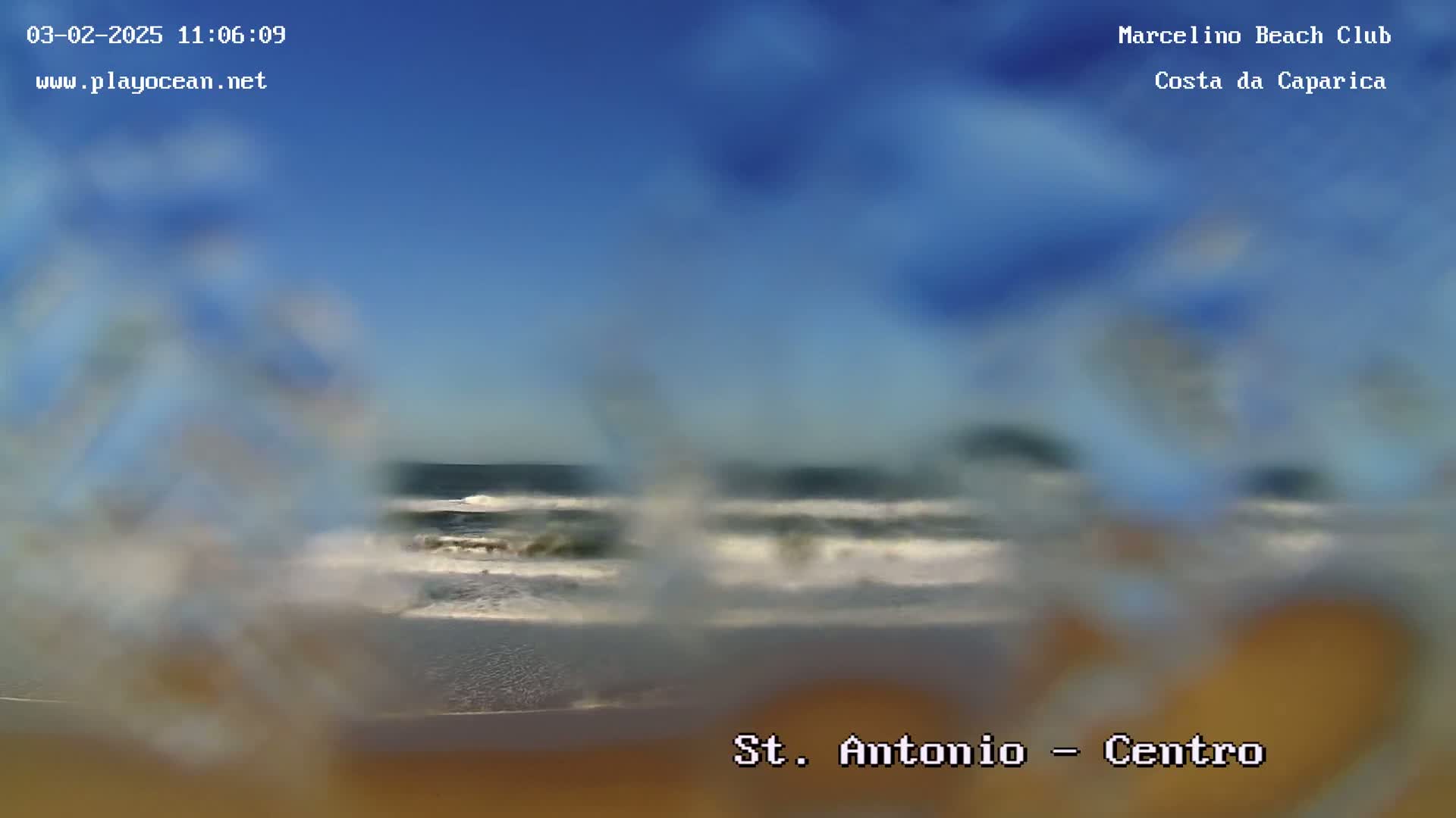 A blurry image shows an ocean beach on a clear day with waves breaking on the shore.