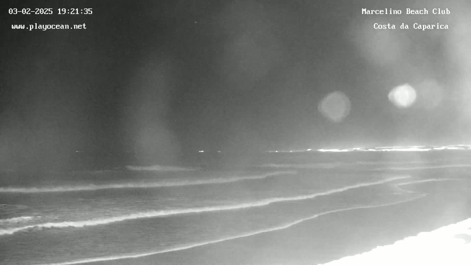 A nighttime view of a dark beach with gently rolling waves under a cloudy sky.