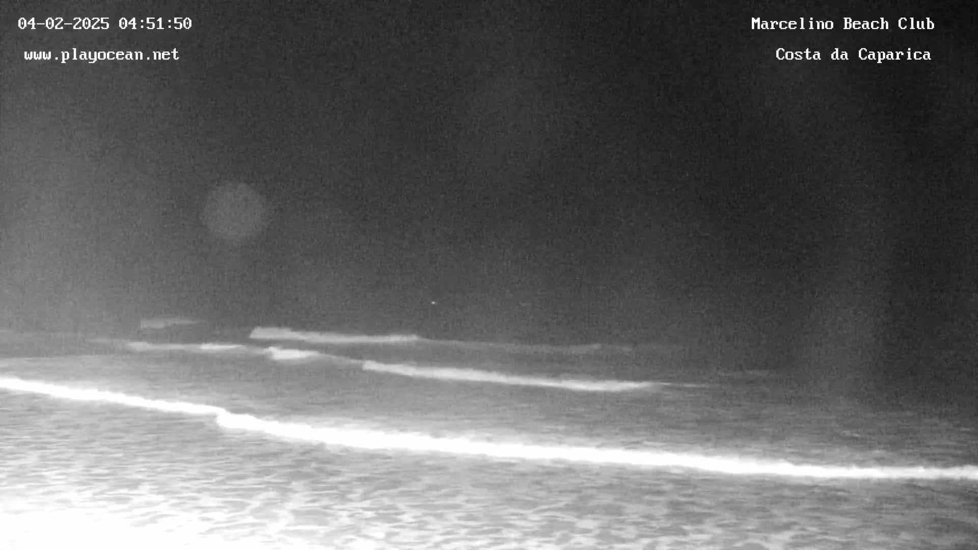 A dark night scene shows gently rolling waves on a beach under a clear, dark sky.