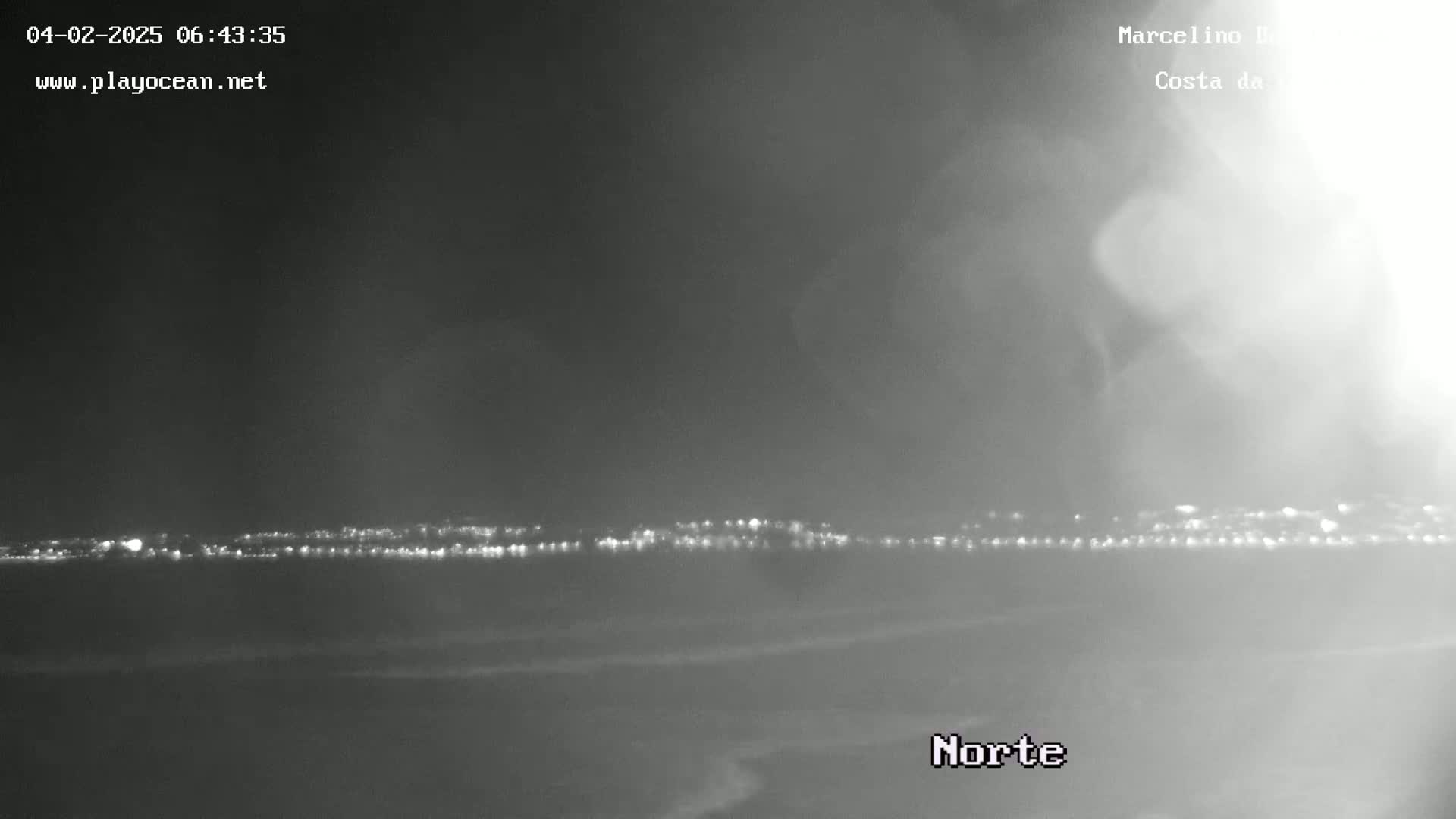 A nighttime view of a distant city skyline across a dark, possibly foggy, body of water.