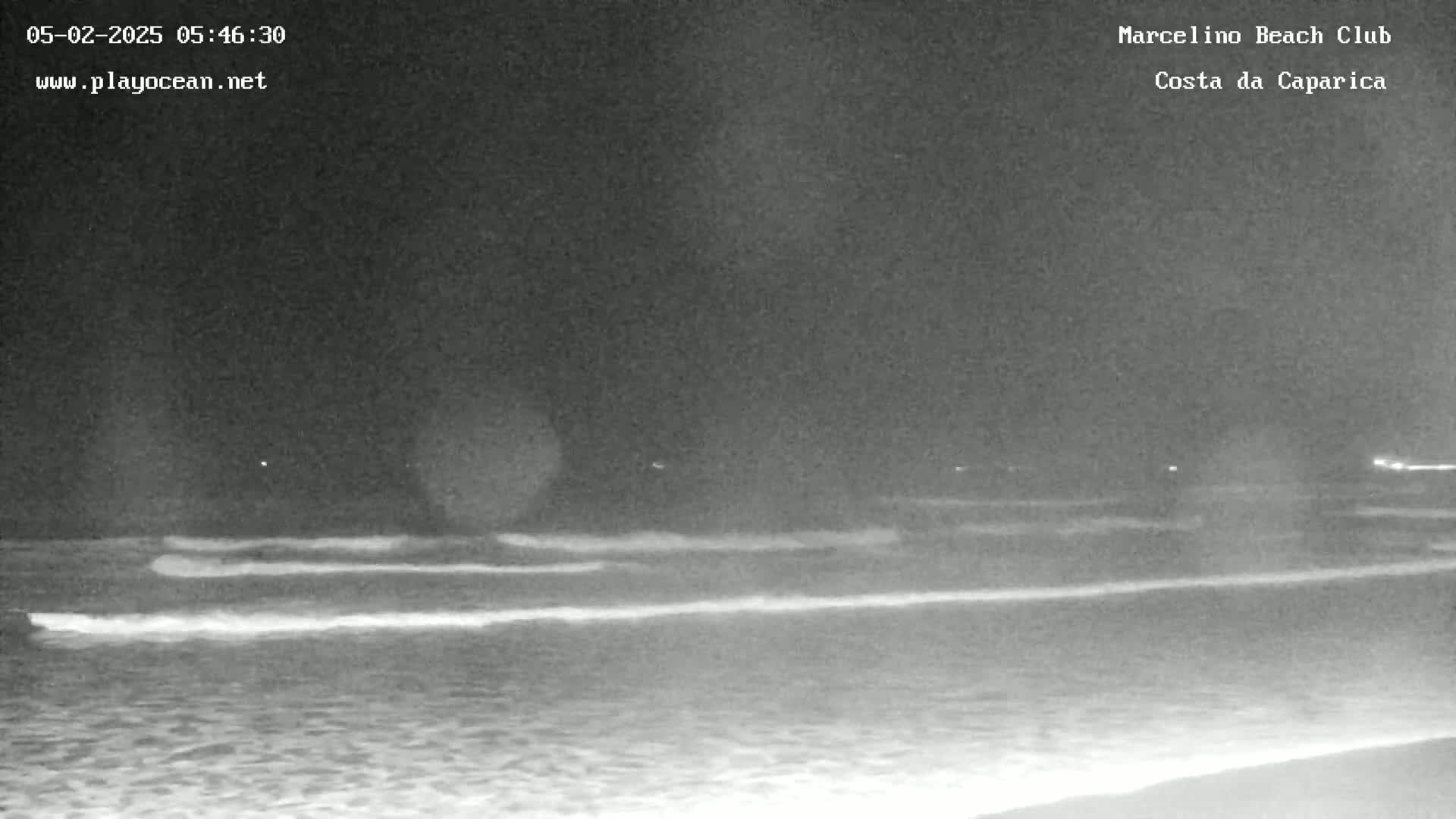A nighttime beach scene shows gentle waves lapping the shore under a dark sky.