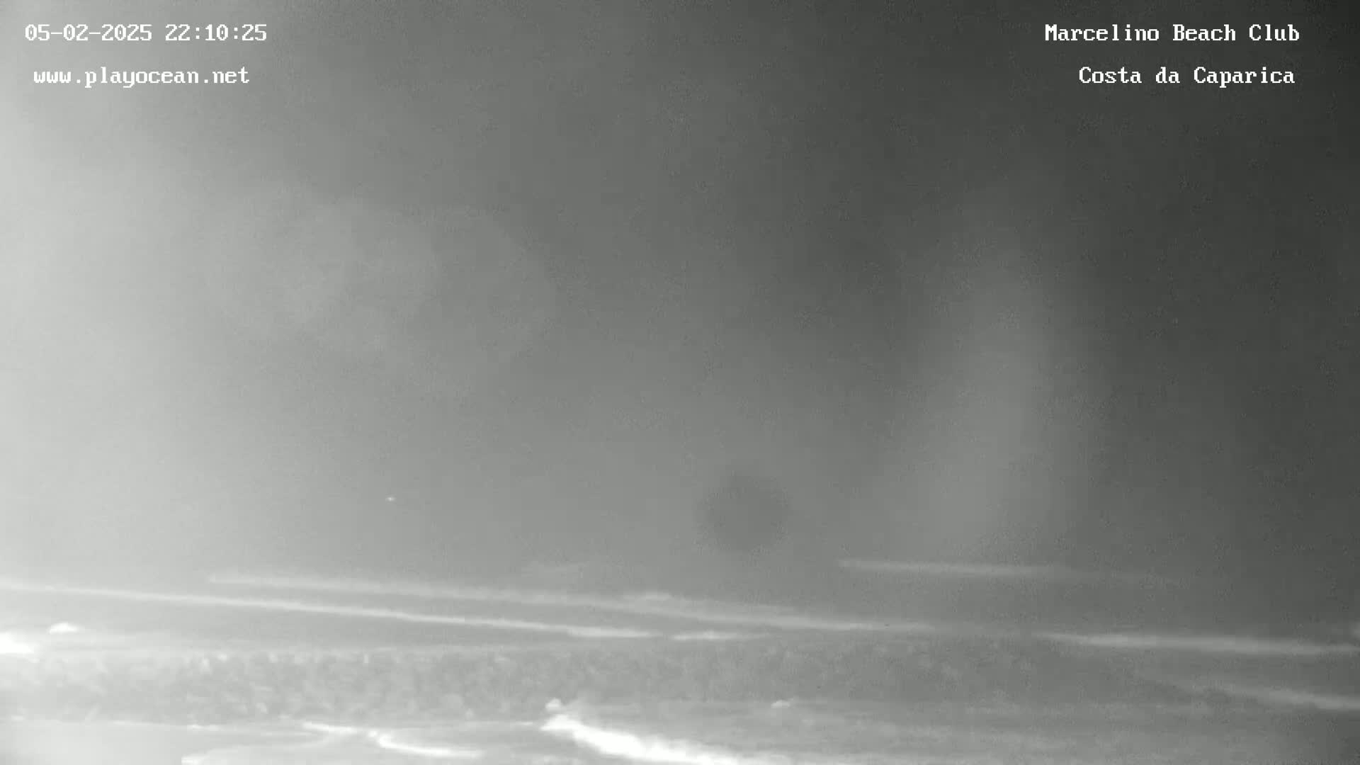 A nighttime, hazy view of a beach with gentle waves lapping the shore.