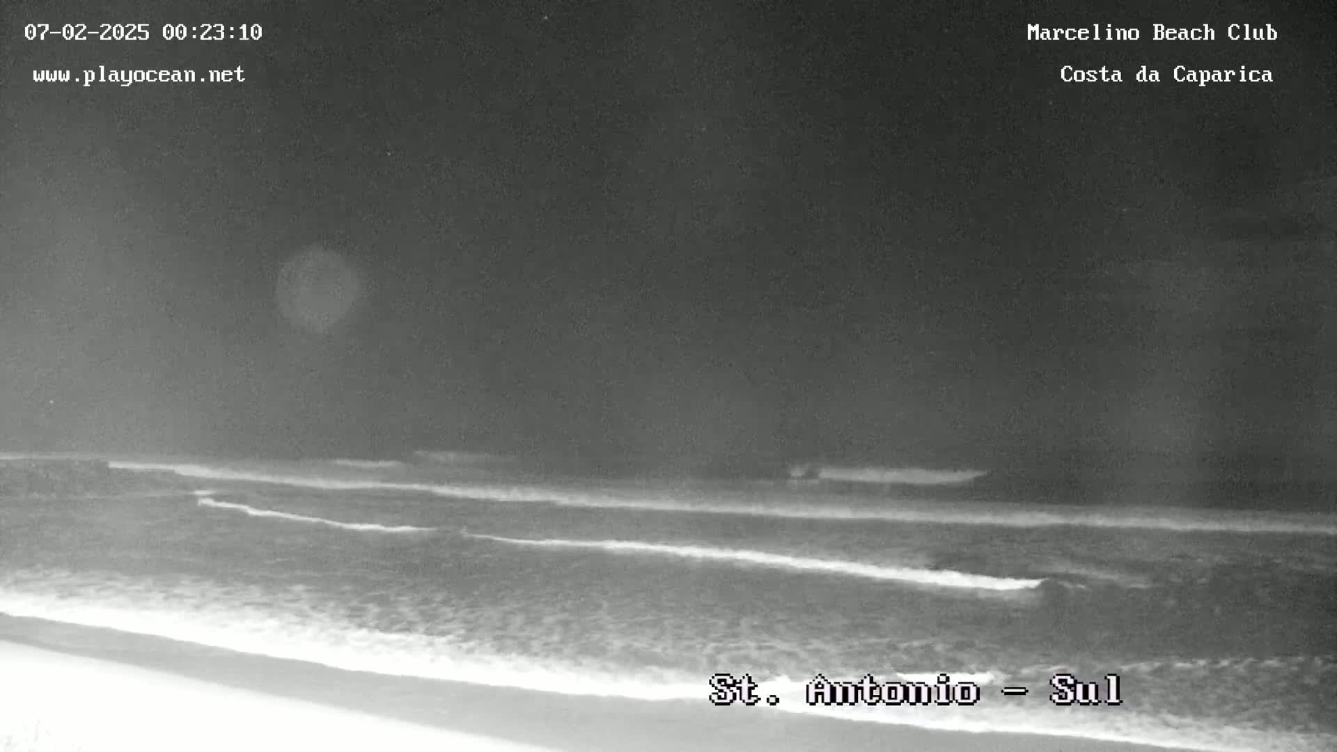 A nighttime, low-light view of a beach with gentle waves lapping the shore under a dark sky.