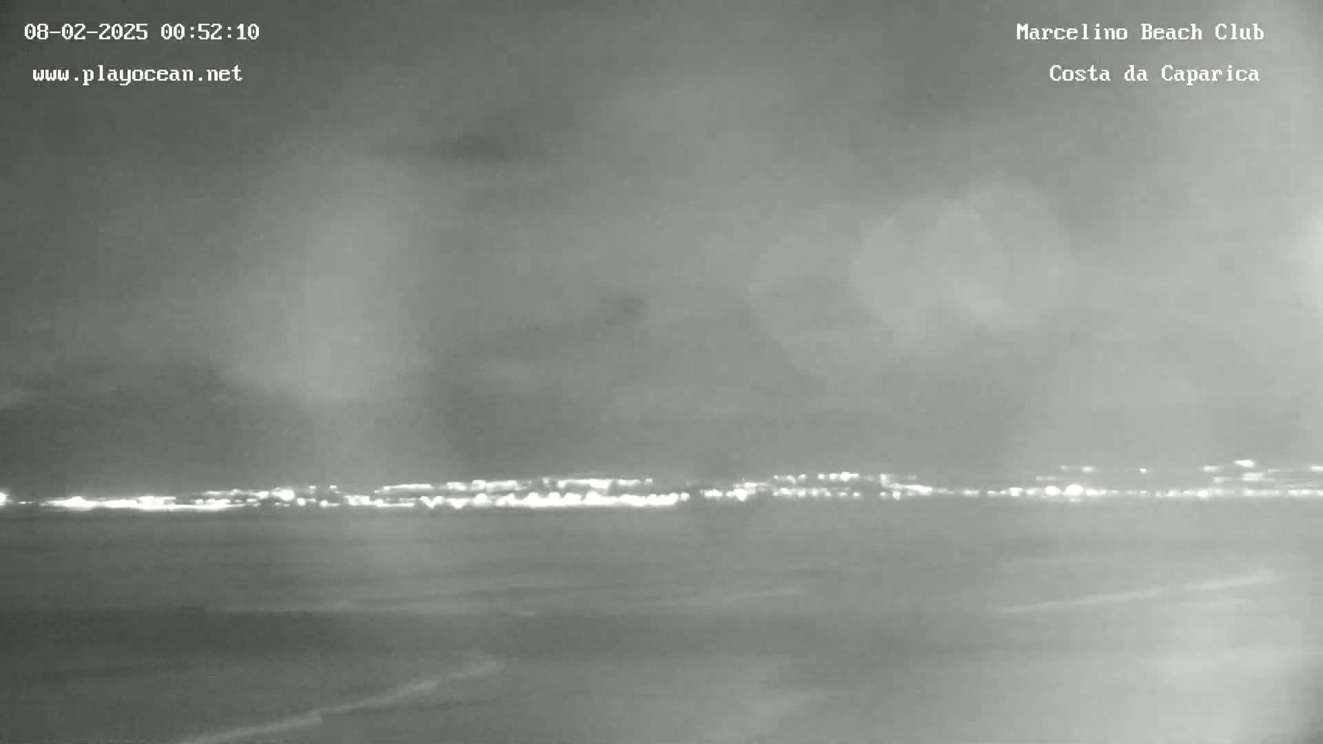 A nighttime, overcast view of a calm body of water with a distant city skyline illuminated.
