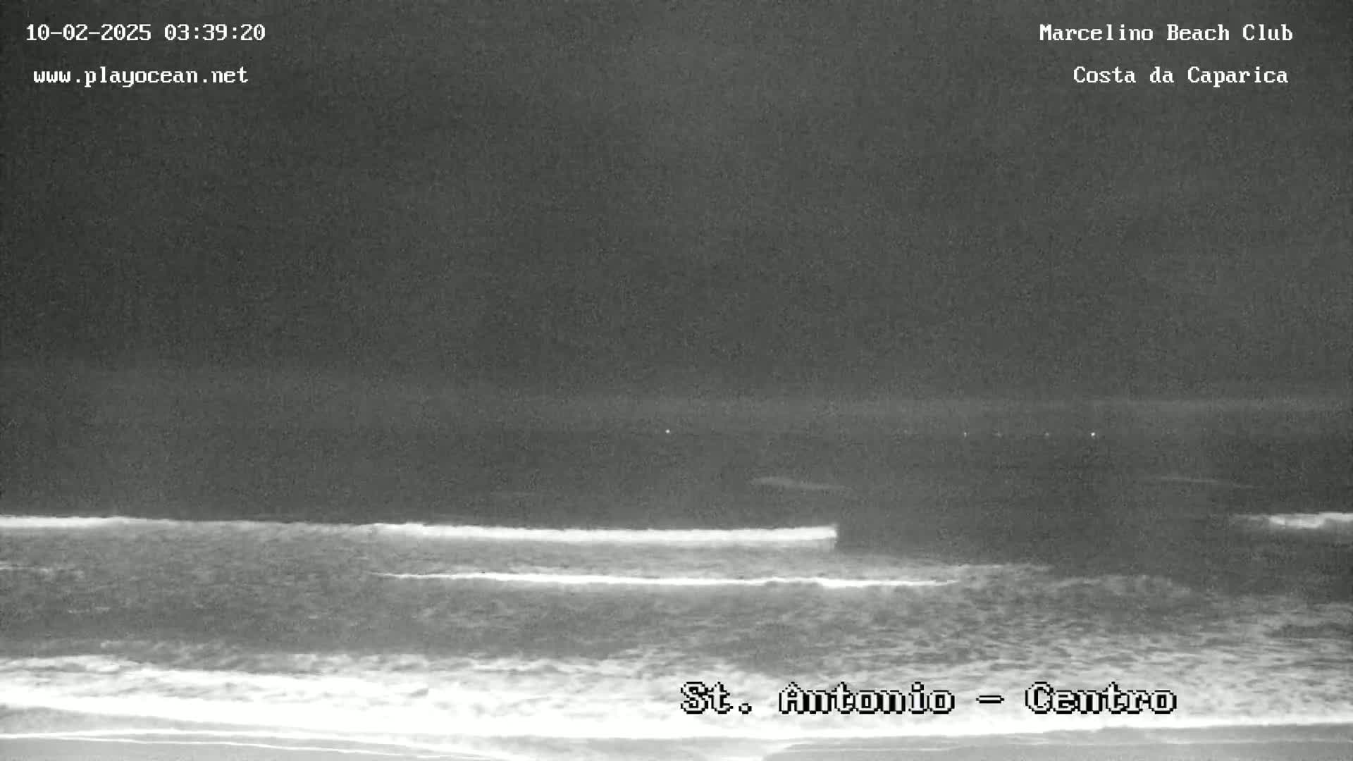A nighttime, low-light view of ocean waves lapping a sandy shore.