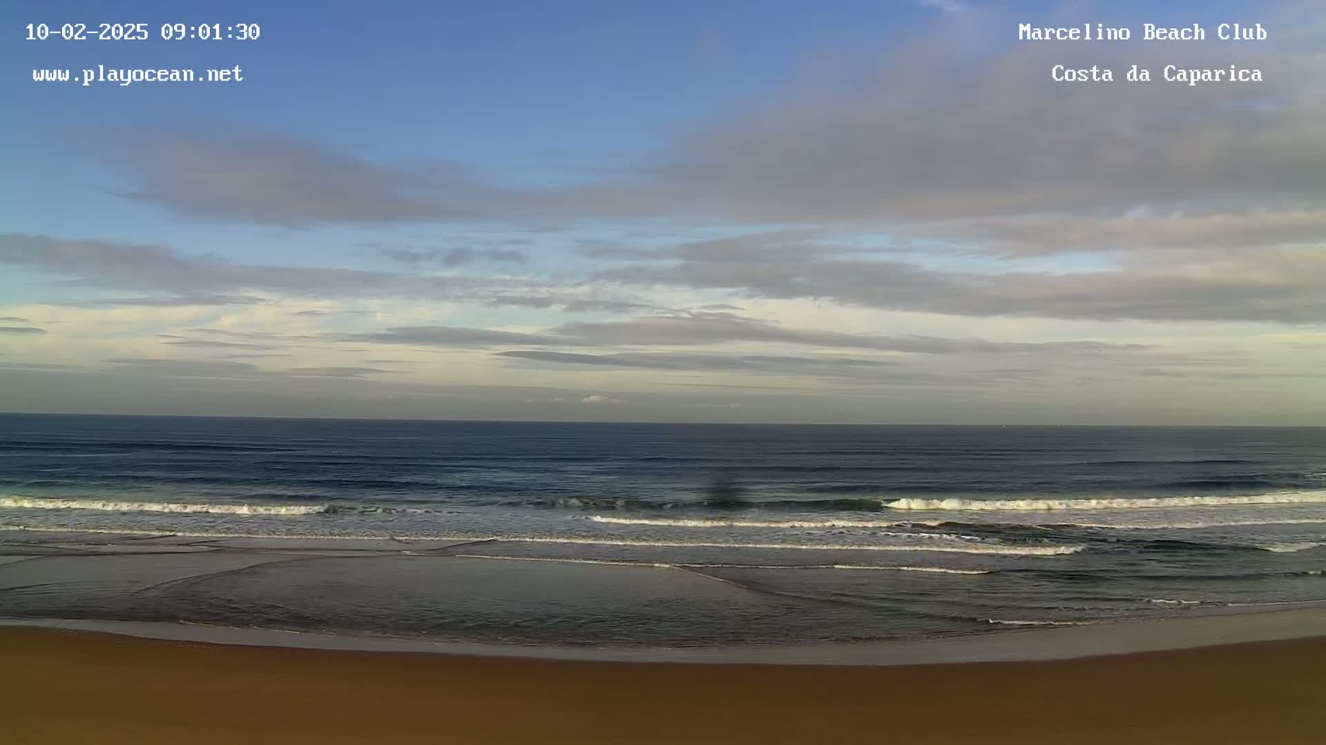 A sandy beach with gentle waves rolling onto the shore under a partly cloudy sky.