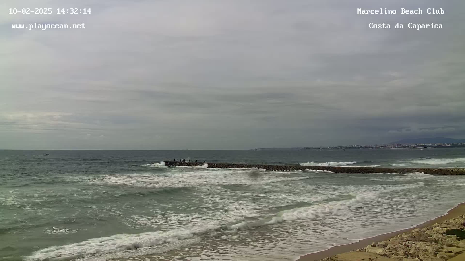 A rocky breakwater juts into a gray, somewhat choppy ocean under a cloudy sky.