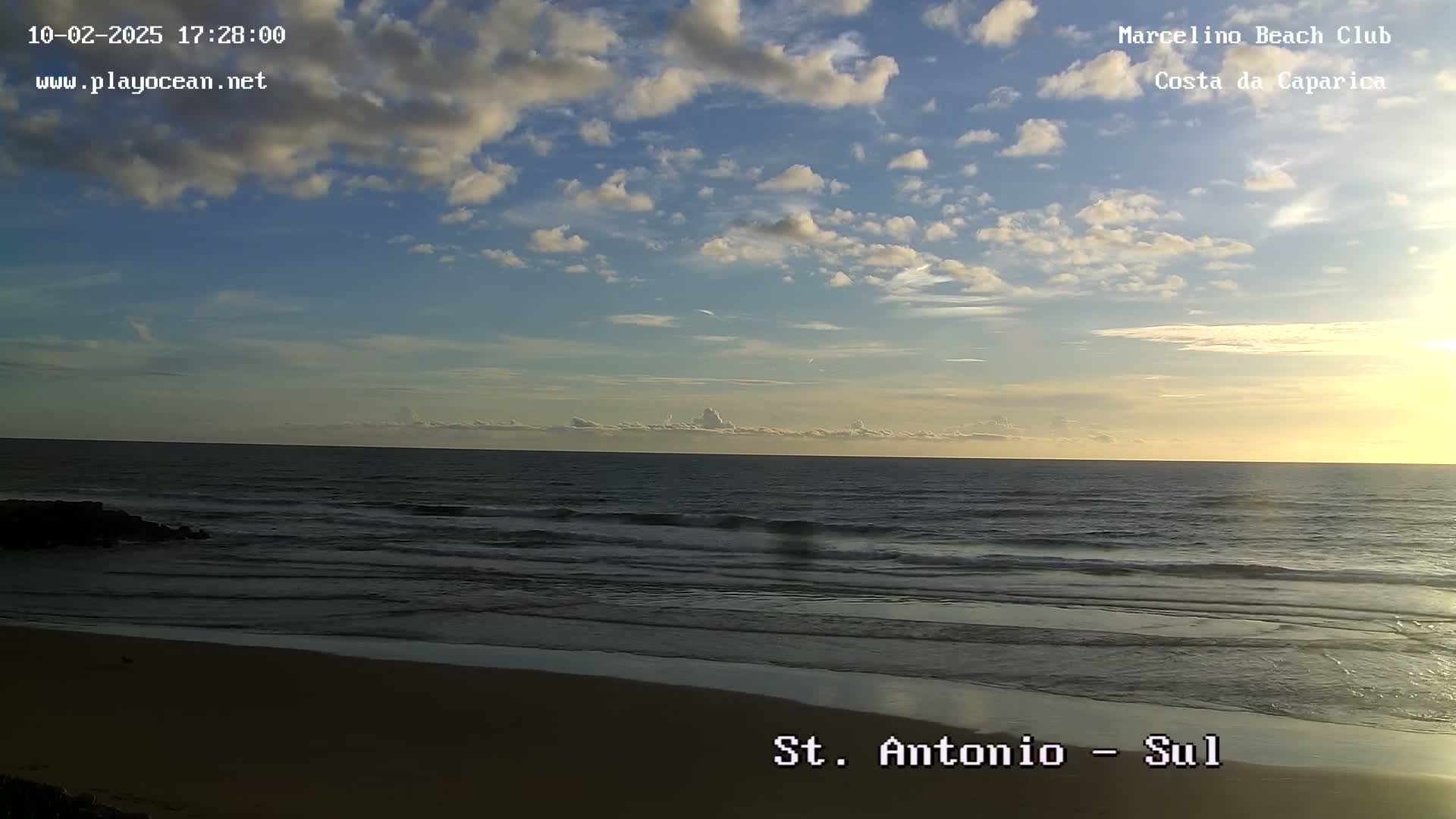 A partly cloudy sunset over a calm ocean with a sandy beach.
