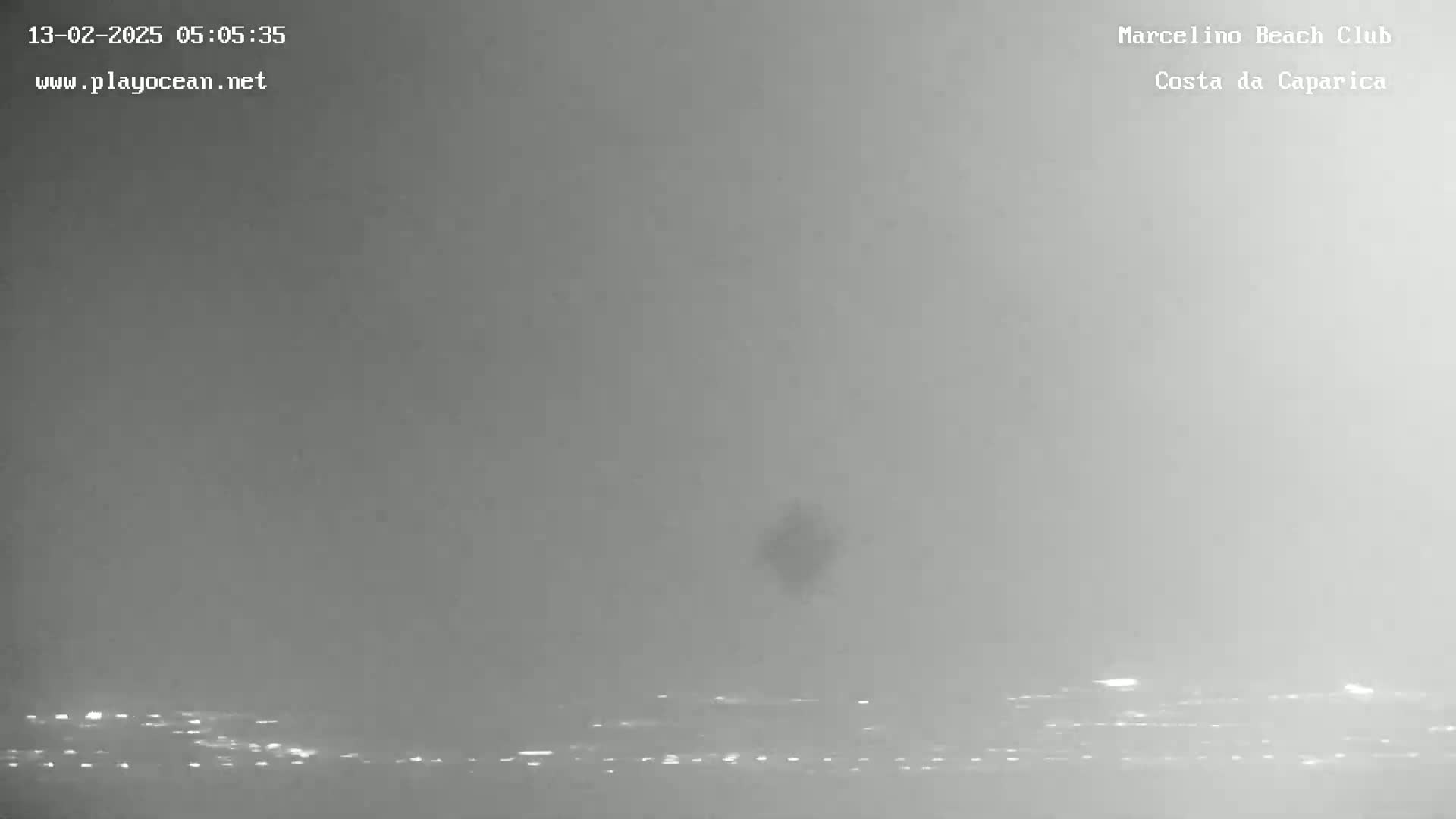 A hazy, overcast day shows a dark shape in the distance over a body of water with a faint line of lights along the horizon.