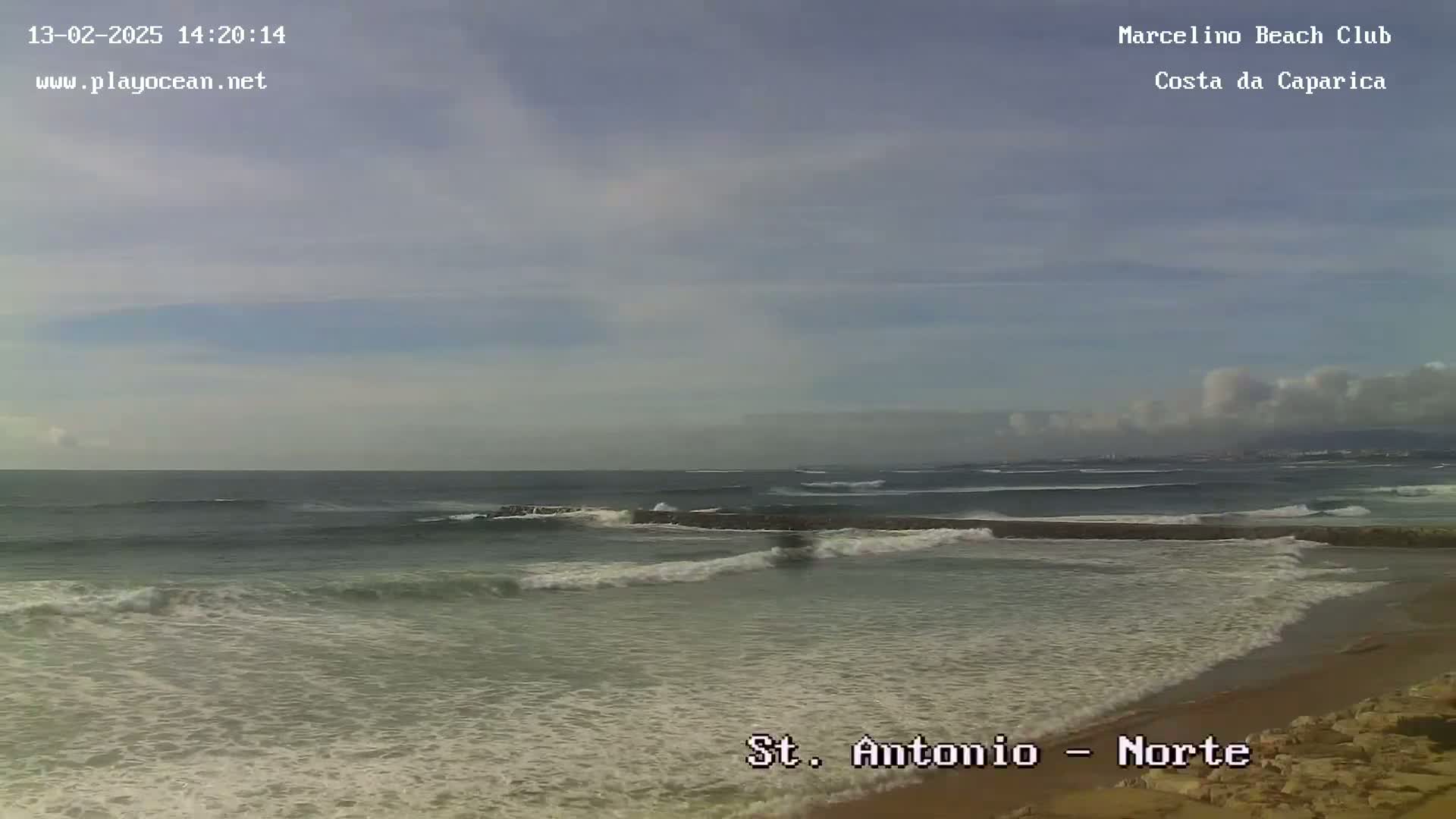 A sandy beach with waves breaking on the shore under a mostly cloudy sky.