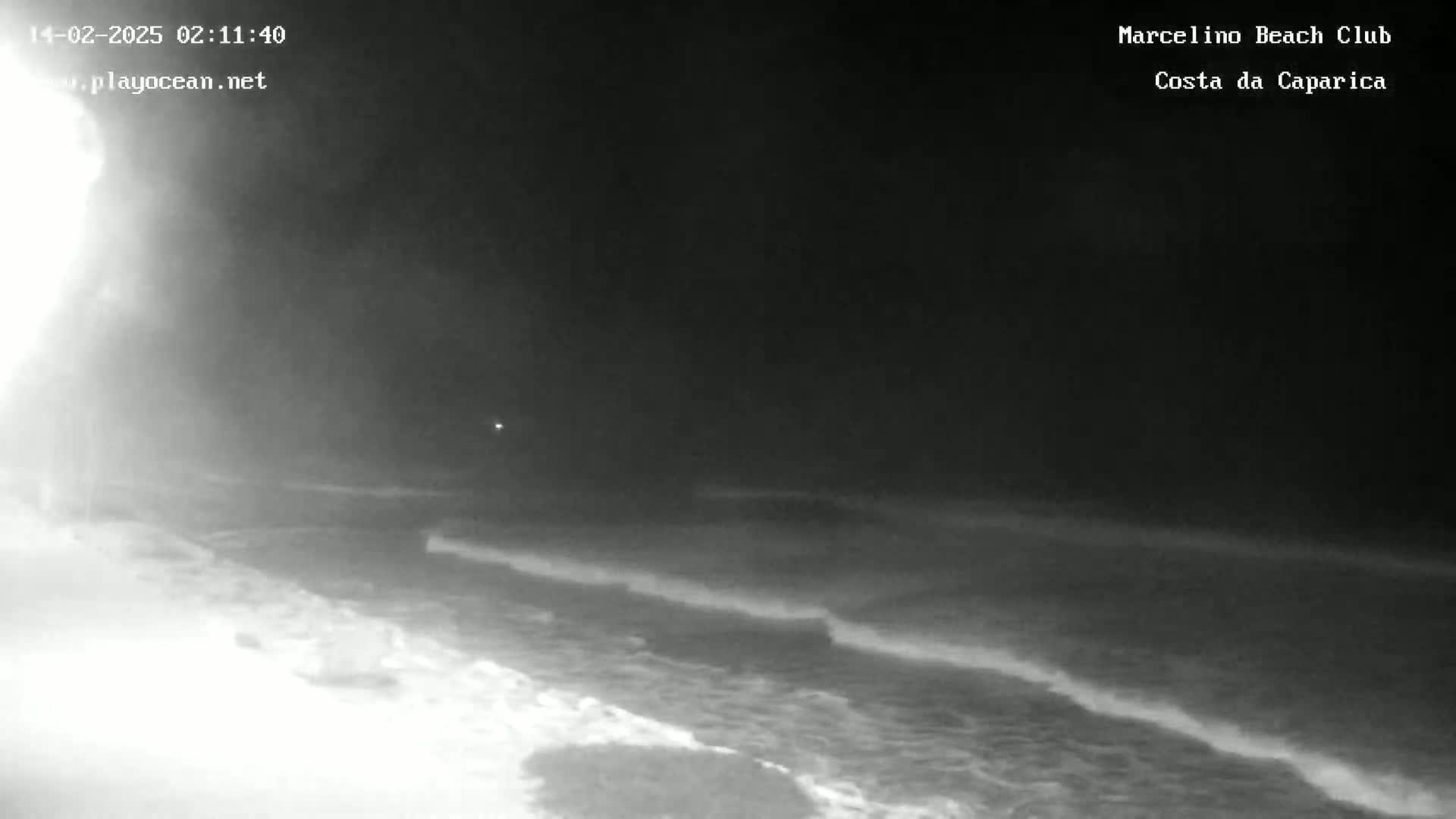 A nighttime, low-light view of a beach with waves gently rolling onto the shore under a dark sky.