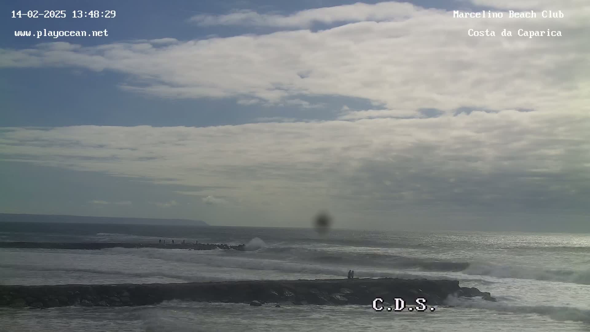 A rocky jetty extends into a choppy ocean under a partly cloudy sky.