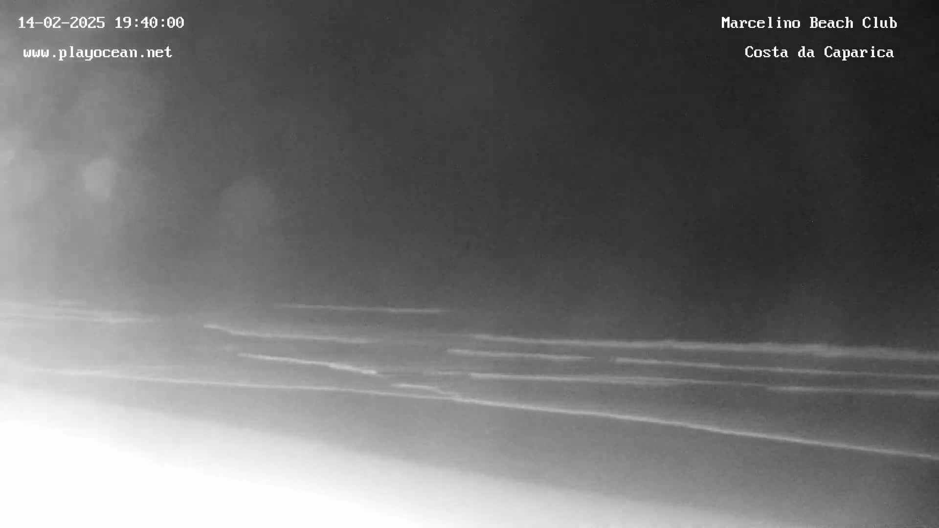 A nighttime, low-light image shows dark sand and small waves on a beach.