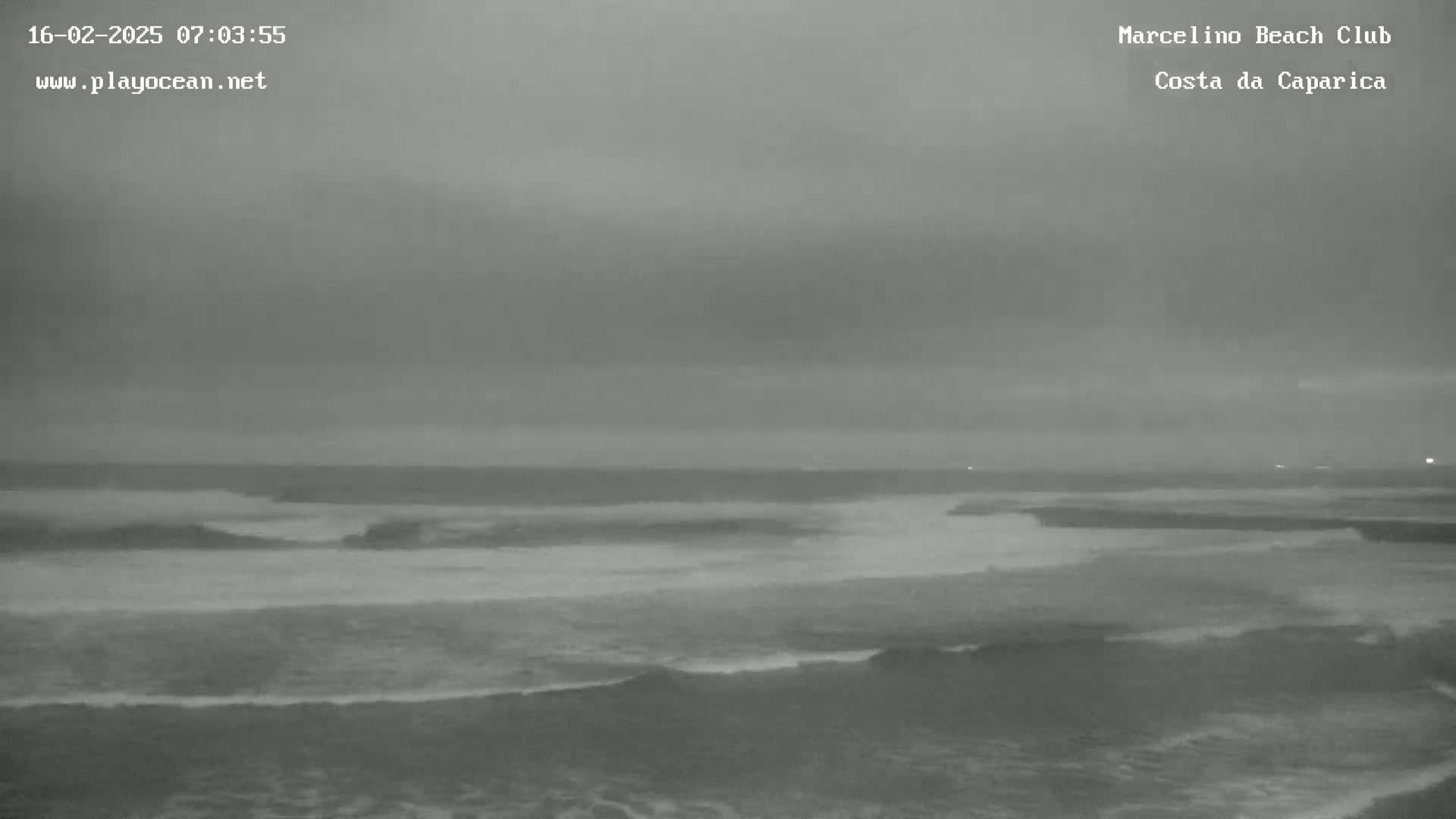 A grayscale image shows an overcast sky over a dark ocean with small waves breaking near the shore.