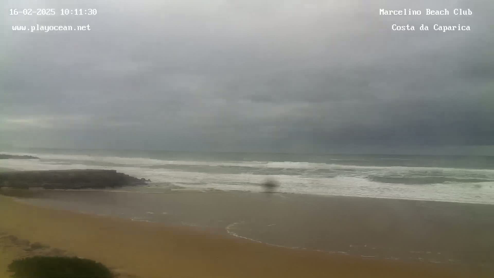 A sandy beach with moderate waves under an overcast sky is shown.