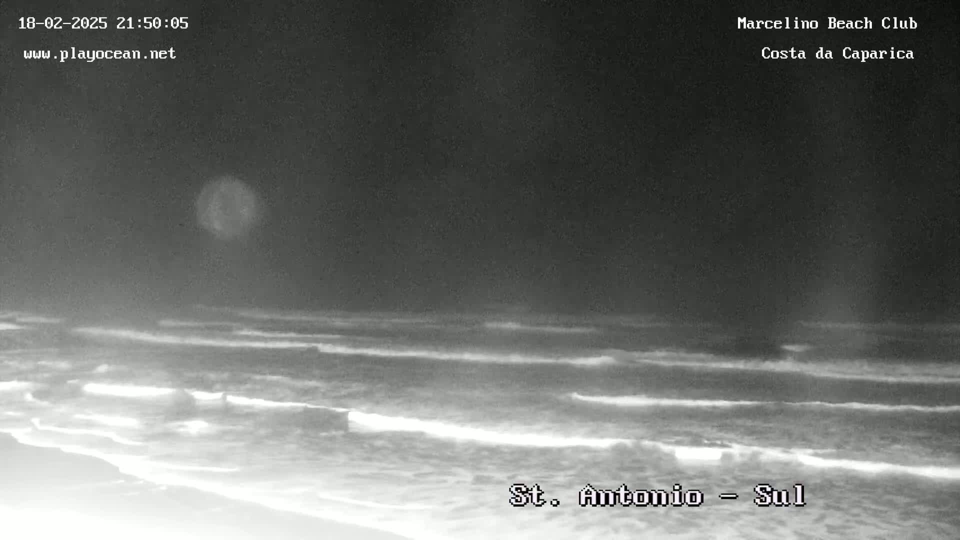 A nighttime, low-light view of gently rolling waves on a beach.