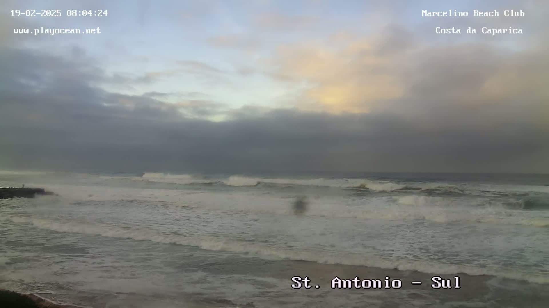 A mostly cloudy sky over a beach with moderately rough waves.