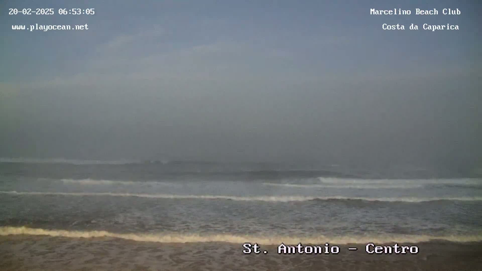 A hazy, overcast day shows a beach with waves rolling onto the shore.