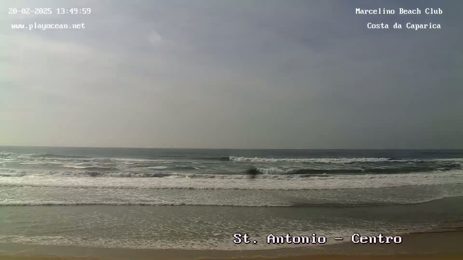 A partly cloudy day shows moderate waves breaking on a sandy beach.