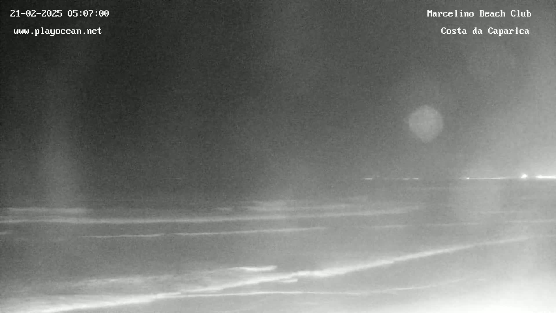 A nighttime view of a dark ocean with small waves under a cloudy sky.