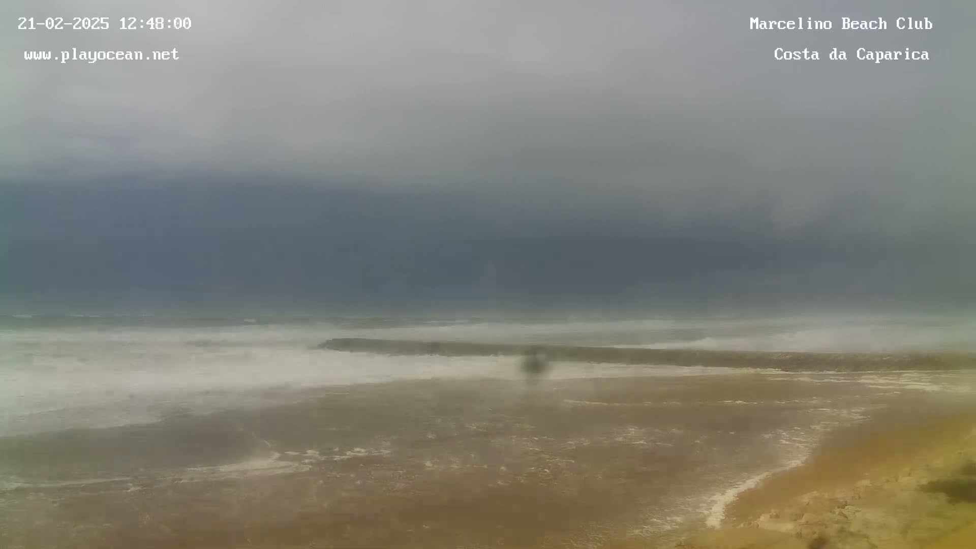 A stormy, overcast day at a beach shows choppy waves crashing near a rock jetty.