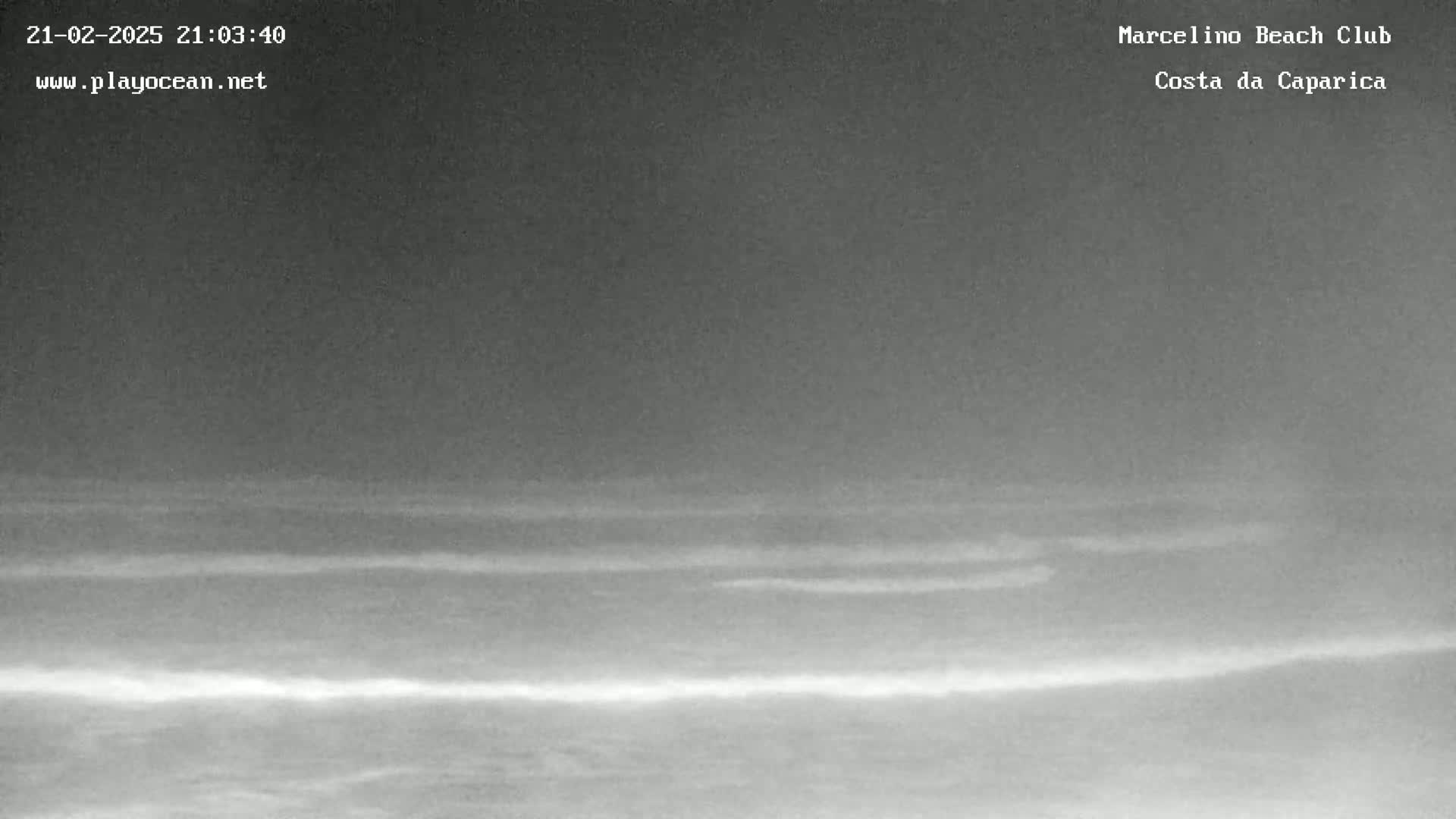 A nighttime, low-light image shows dark, calm ocean waves under a dark sky.