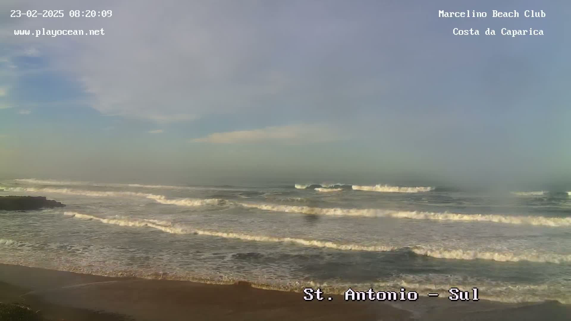 A hazy, overcast day shows moderate waves rolling onto a sandy beach.