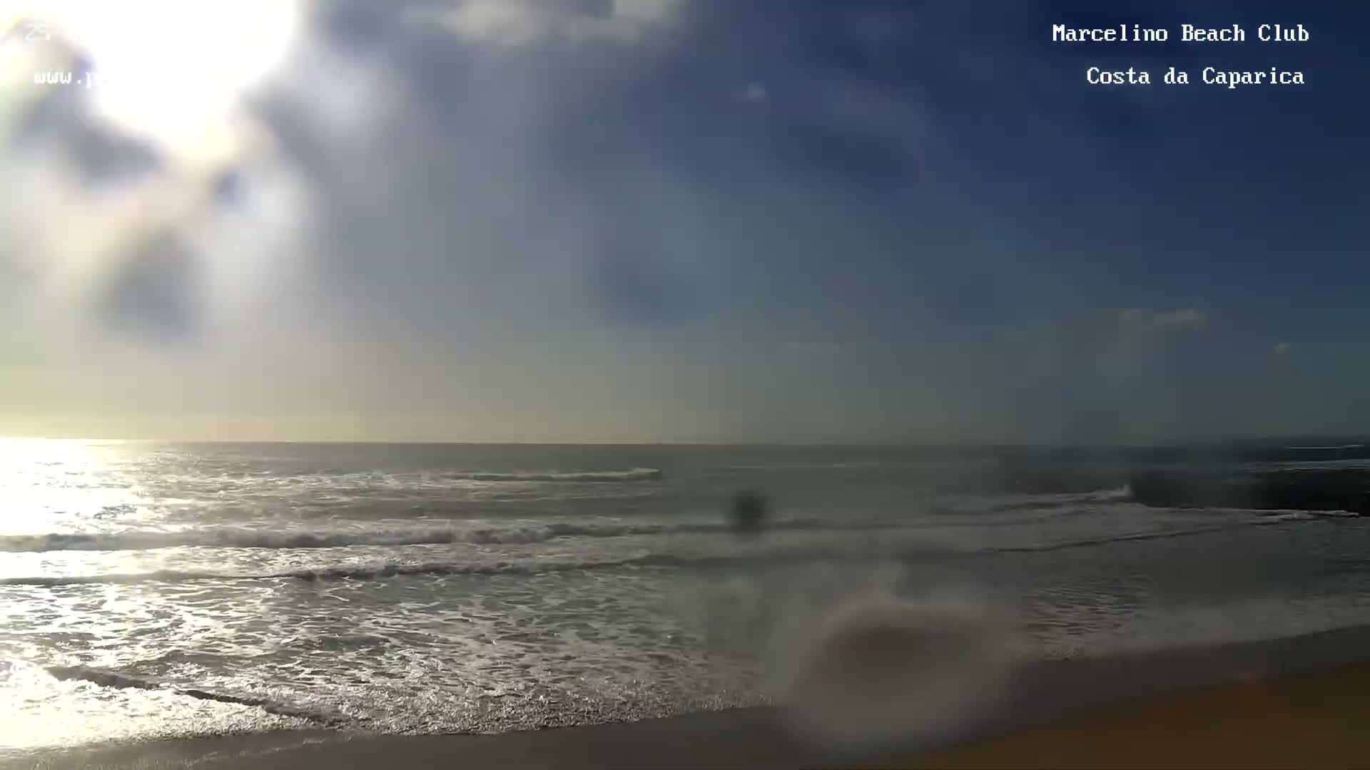 A partly sunny day shows gentle waves breaking on a sandy beach.