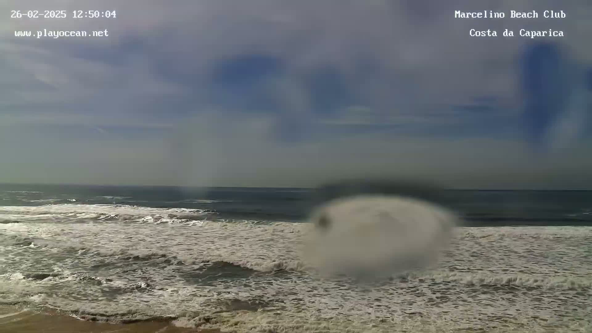 A slightly overcast sky overlooks a beach with moderately sized waves breaking onto the shore.