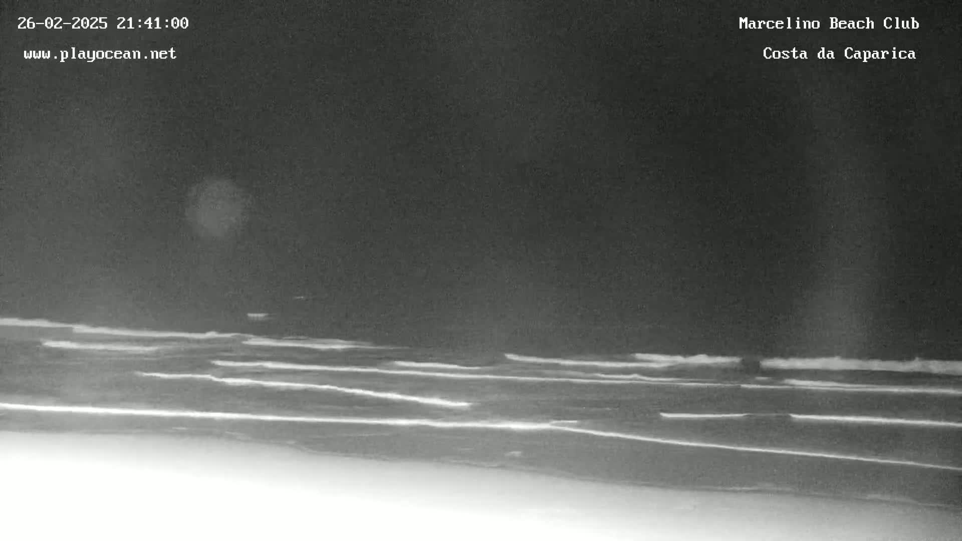 A nighttime view of ocean waves gently breaking on a dark beach under a clear sky.